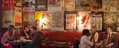 several people sitting at tables in a restaurant with posters on the wall and flooring