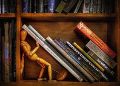 a wooden figurine sitting on top of a book shelf filled with lots of books