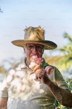 an old man wearing a straw hat and holding flowers in his hand while looking at the camera