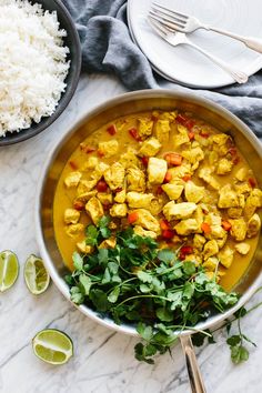 a bowl filled with chicken and vegetables next to rice, cilantro and lime wedges