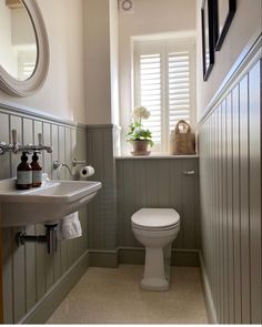 a white toilet sitting next to a sink in a bathroom under a window with shutters