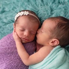 two newborn babies cuddle together on a blue blanket, one is kissing the other