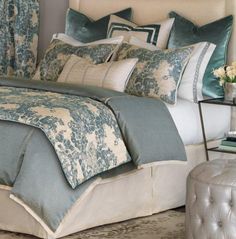 a bed with blue and white comforters in a bedroom next to a footstool