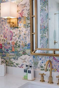 a bathroom sink under a large mirror next to a wall papered with colorful flowers