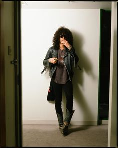 a woman standing in front of a white wall holding a cell phone to her ear