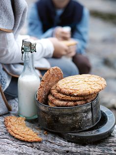 some cookies and milk on a table next to a person sitting down with a bottle of milk