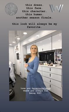 a woman in a blue dress standing next to a kitchen with white cabinets and drawers