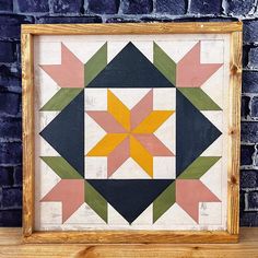 a wooden frame holding a colorful quilt on a shelf next to a blue brick wall