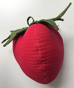 a close up of a red object on a white surface with a green leaf attached to it