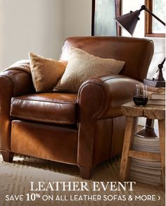 a brown leather chair sitting in front of a window next to a table with a glass of wine on it