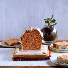 a piece of cake sitting on top of a cutting board next to two plates and a potted plant