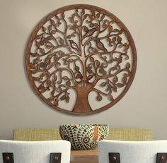 a wooden wall hanging with a tree design on it's face and two chairs in front of it