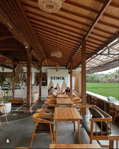 an outdoor restaurant with wooden tables and chairs under a covered area that has rice fields in the background