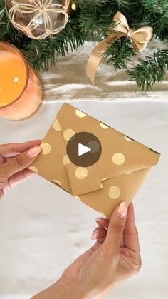 two hands holding an envelope with gold polka dots on it, next to a christmas tree