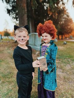 two children dressed up in costumes standing next to each other with their faces painted like cats