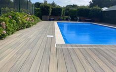 an empty swimming pool in the middle of a wooden decked area with purple flowers