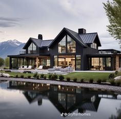 a large black house sitting on top of a lush green field next to a lake