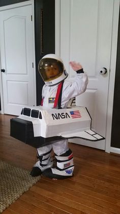 a small child dressed in an astronaut suit holding a box with the nasa written on it