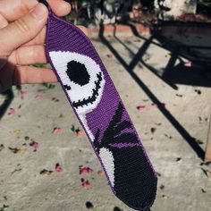 a hand holding up a purple knitted tie with an evil eyeball on it