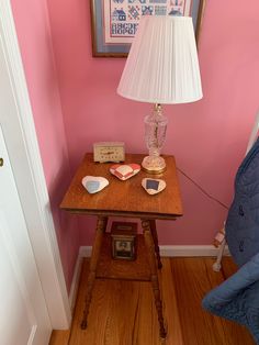 a wooden table topped with a lamp next to a pink wall