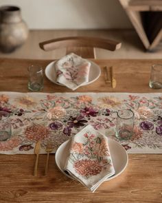 a place setting on a wooden table with floral napkins and gold cutleryware