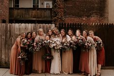 a group of women standing next to each other in front of a wooden fence holding bouquets