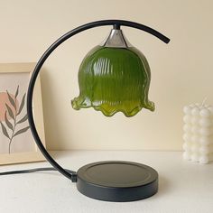 a green lamp sitting on top of a table next to a white vase and framed photograph