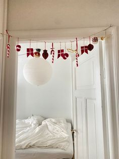 an open door leading to a small bed in a room with christmas decorations hanging from the ceiling