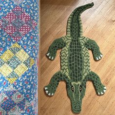 a crocheted alligator rug sitting on top of a wooden floor next to a quilt