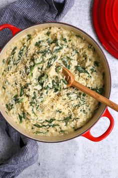 a pot filled with rice and spinach on top of a table next to a red pan