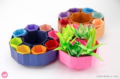 several different colored origami flower pots on a white surface with one plant in the middle