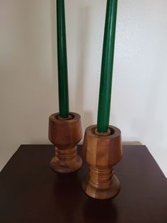 two wooden vases with green candles in them on top of a brown table next to a white wall