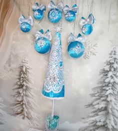 a blue christmas tree surrounded by ornaments in front of a snow covered forest background with pine trees