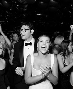 a man and woman standing in front of a crowd at a party with confetti hanging from the ceiling