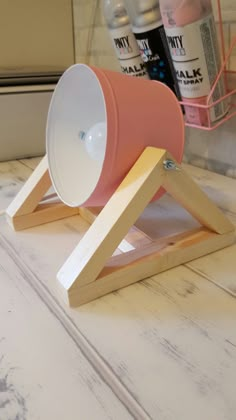 a pink and white cup sitting on top of a wooden stand next to some bottles