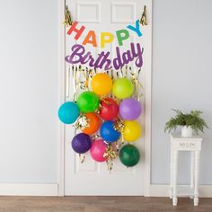 a bunch of balloons are hanging on the door with a happy birthday sign in the background