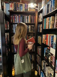 a woman standing in front of a bookshelf holding a book and looking at it