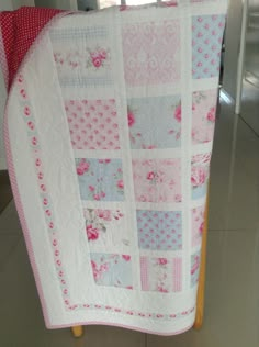 a pink and blue quilt is hanging on a wooden stand in front of a door