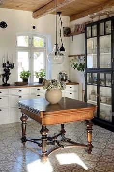 an old fashioned kitchen with white cabinets and wooden table in front of glass fronted cupboards