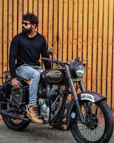 a man sitting on top of a motorcycle next to a wooden fence and wearing sunglasses