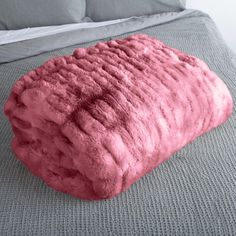 a large pink blanket on top of a bed next to pillows and a night stand