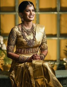 a woman in a gold sari sitting on a bench with her hands clasped to her chest