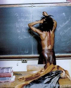 a man standing in front of a blackboard with writing on it and his back to the camera