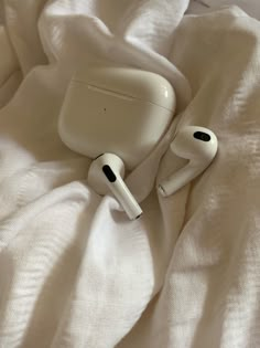 an apple airpods laying on top of a white sheet covered bed with the covers pulled down