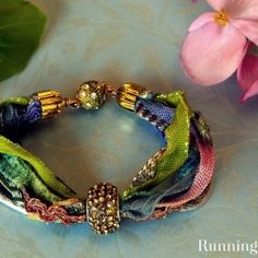 two bracelets are sitting next to pink flowers on a blue surface with green leaves