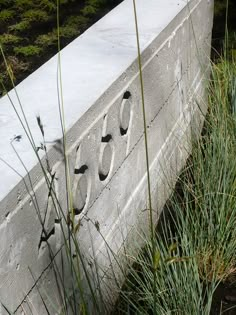 a cement bench with numbers on it and grass growing next to it in the foreground