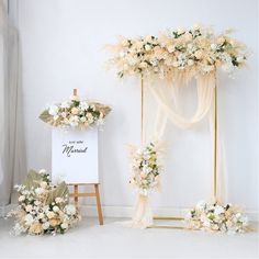 a white and gold wedding set up with flowers on the floor next to an easel