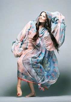 a woman in a blue and pink dress is posing for a photo with her hands behind her head