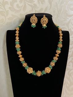 The Nakshi Balls & Green Beads Necklace is a traditional Indian jewelry piece, often inspired by ancient and classical designs These are intricately handcrafted gold beads, commonly found in traditional South Indian jewelry. Nakshi work refers to the detailed carving or embossing of figures, motifs, or patterns, often featuring floral designs, deities, or temple architecture. These gold balls are usually spherical, hollow, and exhibit high craftsmanship with a textured, antique finish. The green Gold Beaded Kundan Necklace As Gift, Bohemian Gold Temple Necklace With Intricate Design, Spiritual Necklaces With Gemstone Beads For Festive Season, Spiritual Kundan Necklace For Puja With Intricate Design, Green Jewelry With Intricate Design For Puja, Gold Temple Necklace With Round Beads, Gold Beaded Necklace With Oval Gemstone Beads, Gold Bohemian Temple Necklace With Intricate Design, Traditional Ceremonial Temple Necklace With Intricate Design