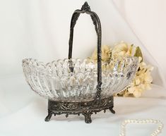 an antique glass basket with handle and beaded handles on a stand next to flowers